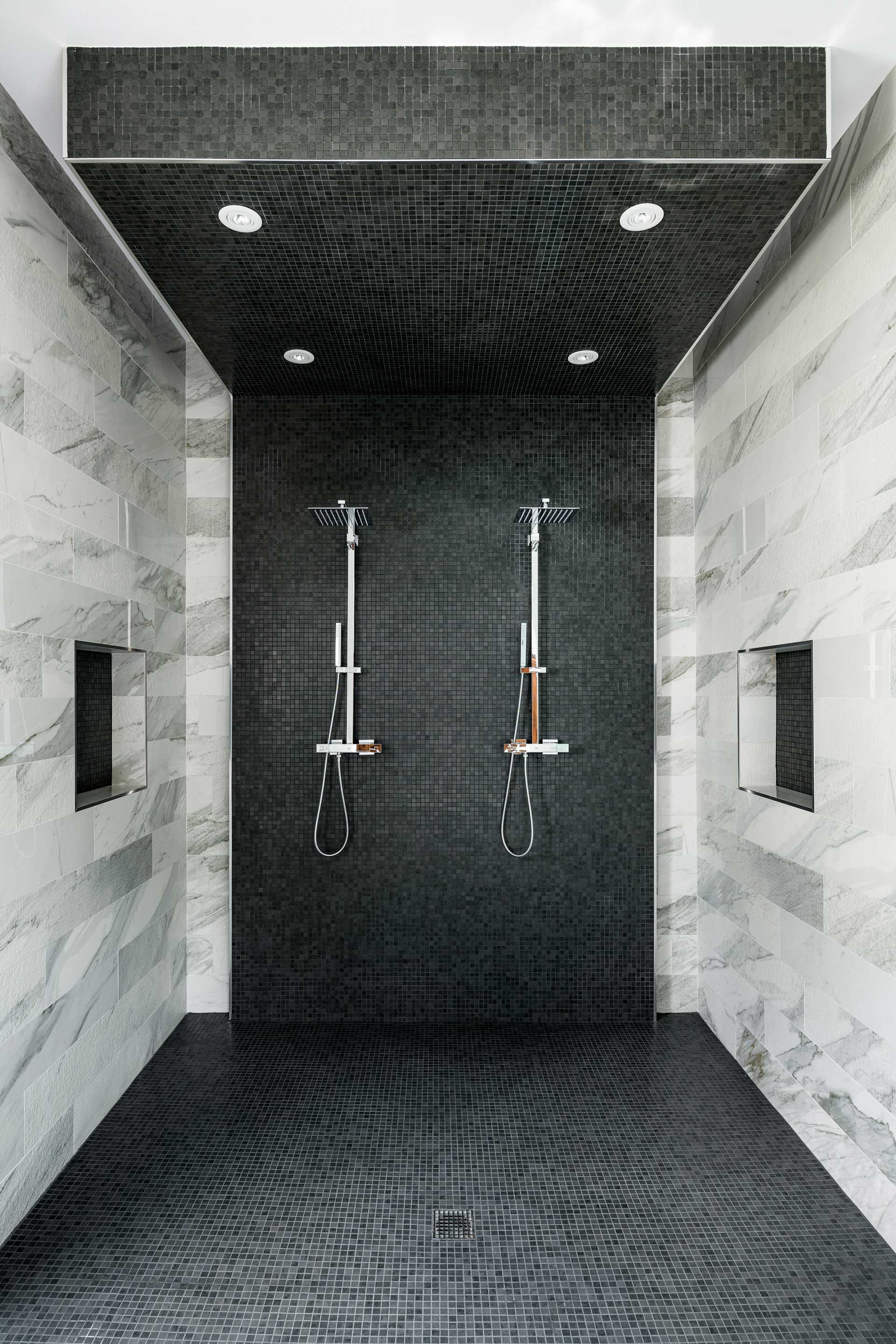 a shower with black tile walls and a couple shower heads