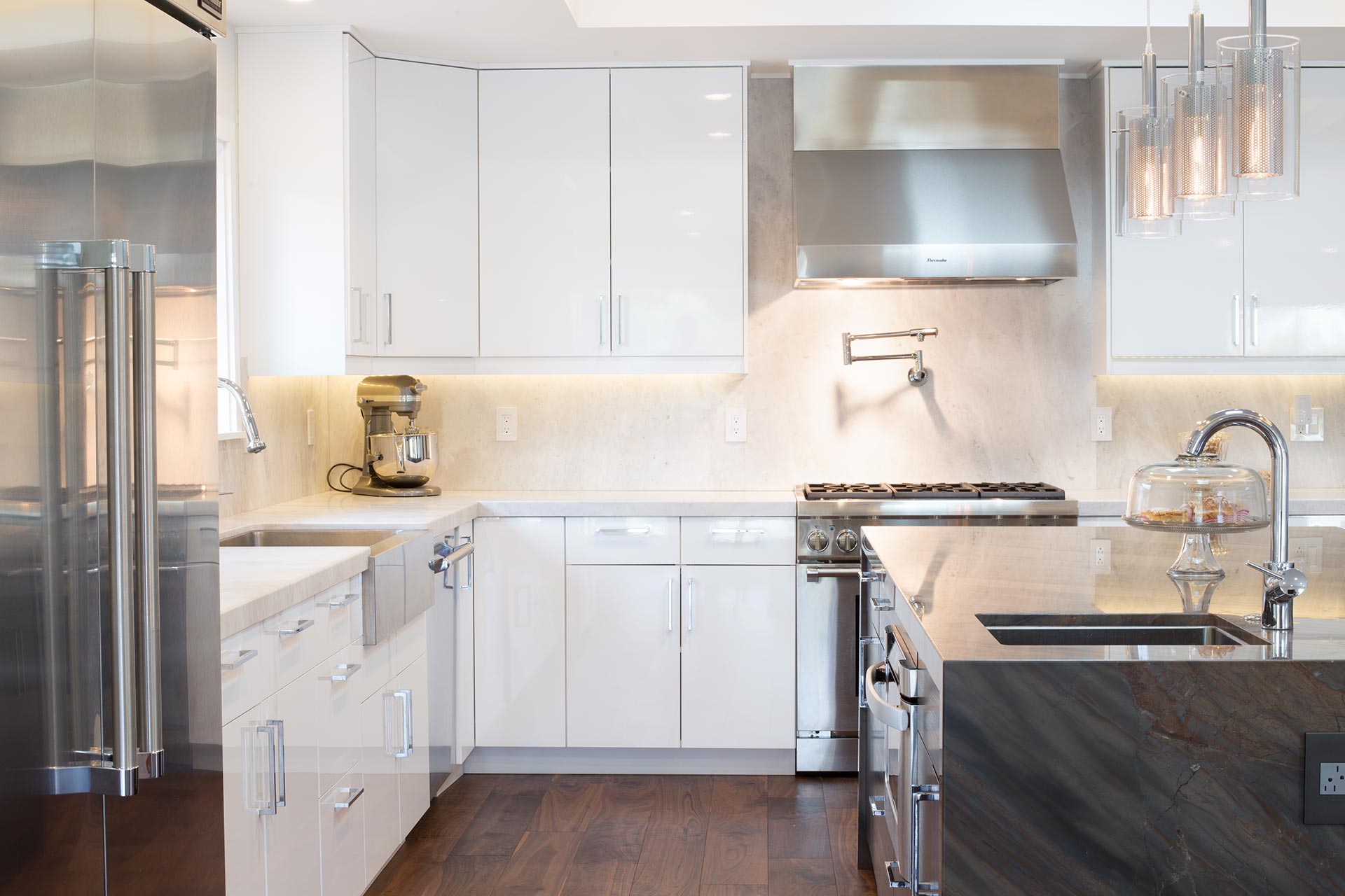 Modern kitchen with glossy white cabinets, stainless steel appliances, dark wood floor, and a large island with a built-in sink.