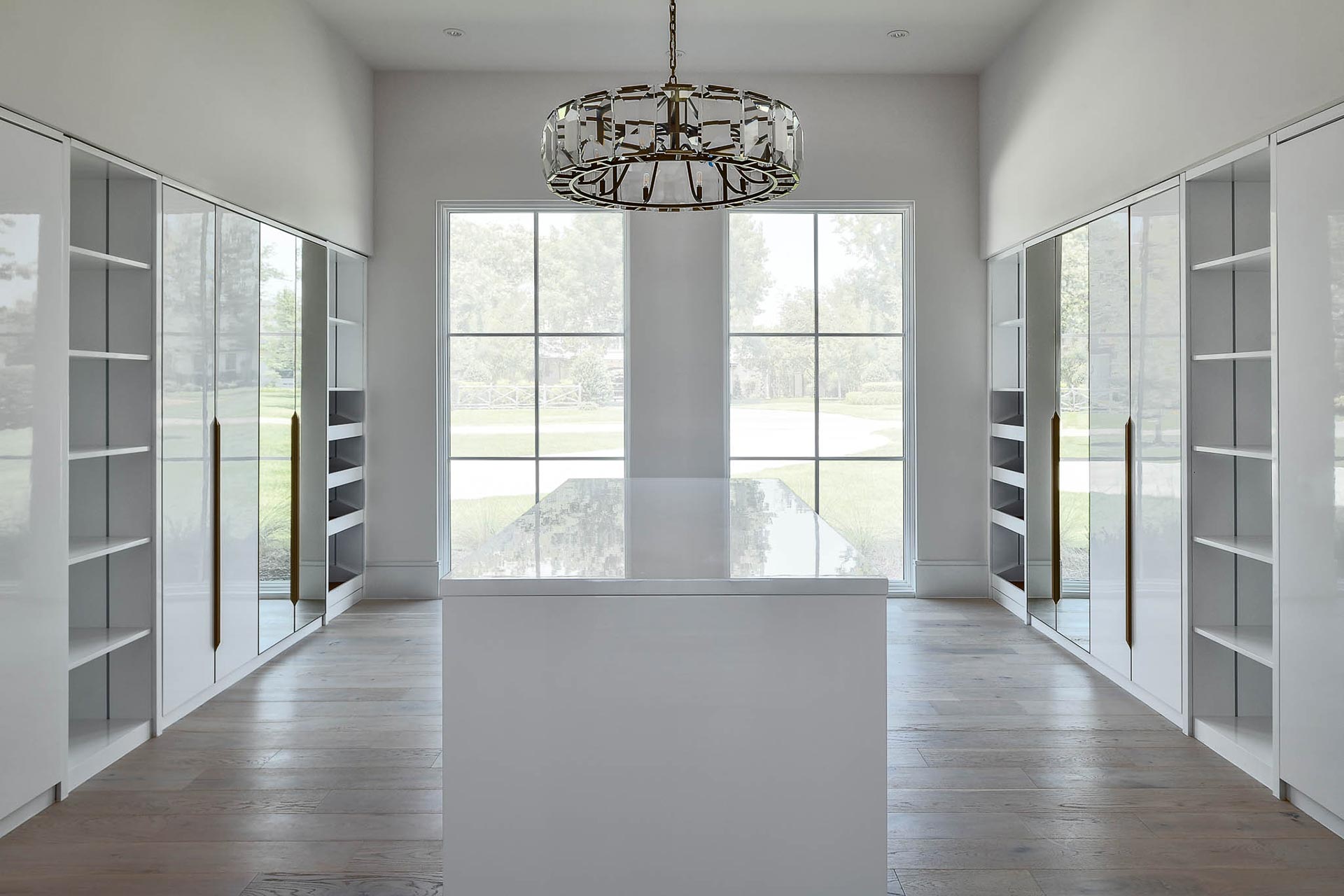 A luxurious walk-in closet featuring elegant white cabinets and a stunning chandelier overhead.