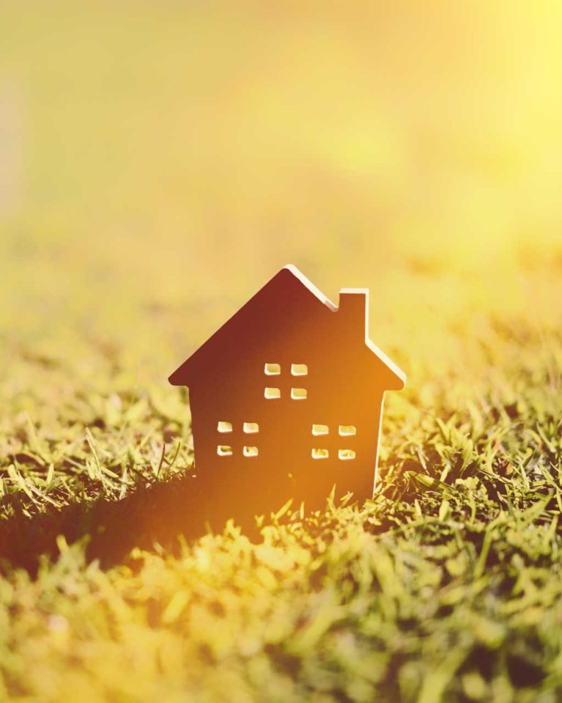 Copy space of home and life concept. Small model home on green grass with sunlight abstract background.